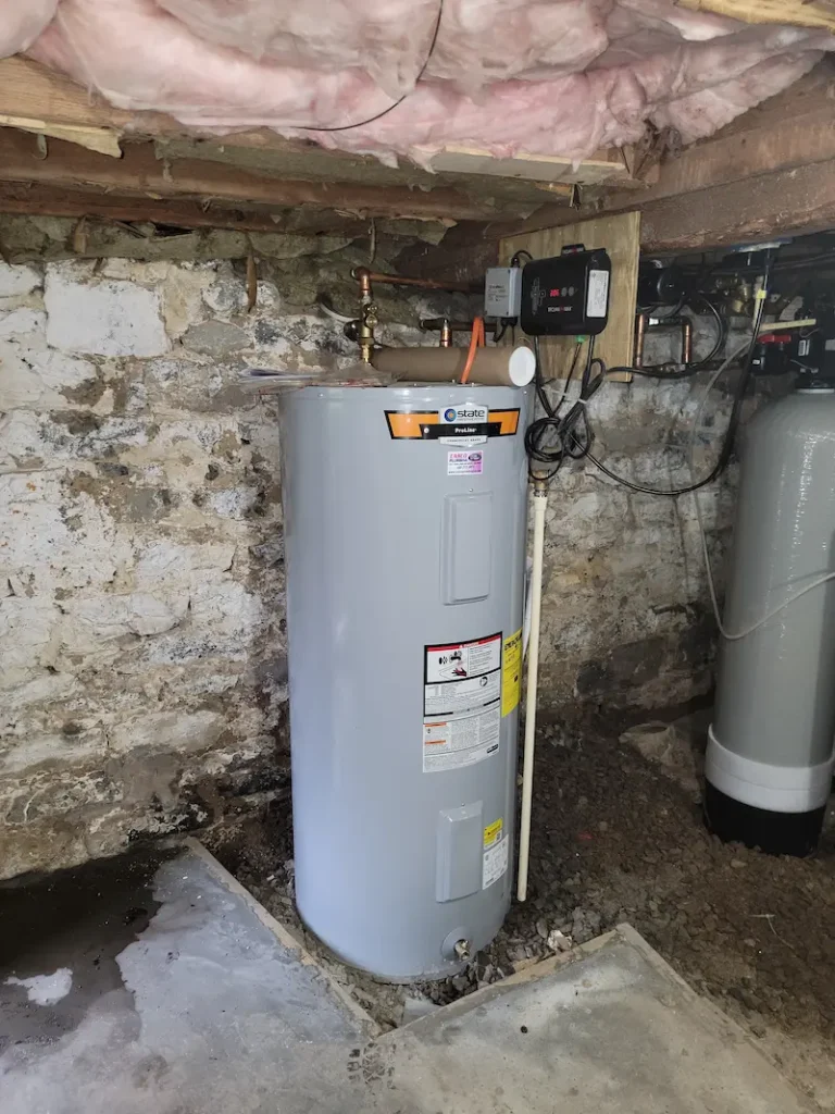 Gray water heater tank in a basement setting with pipes.